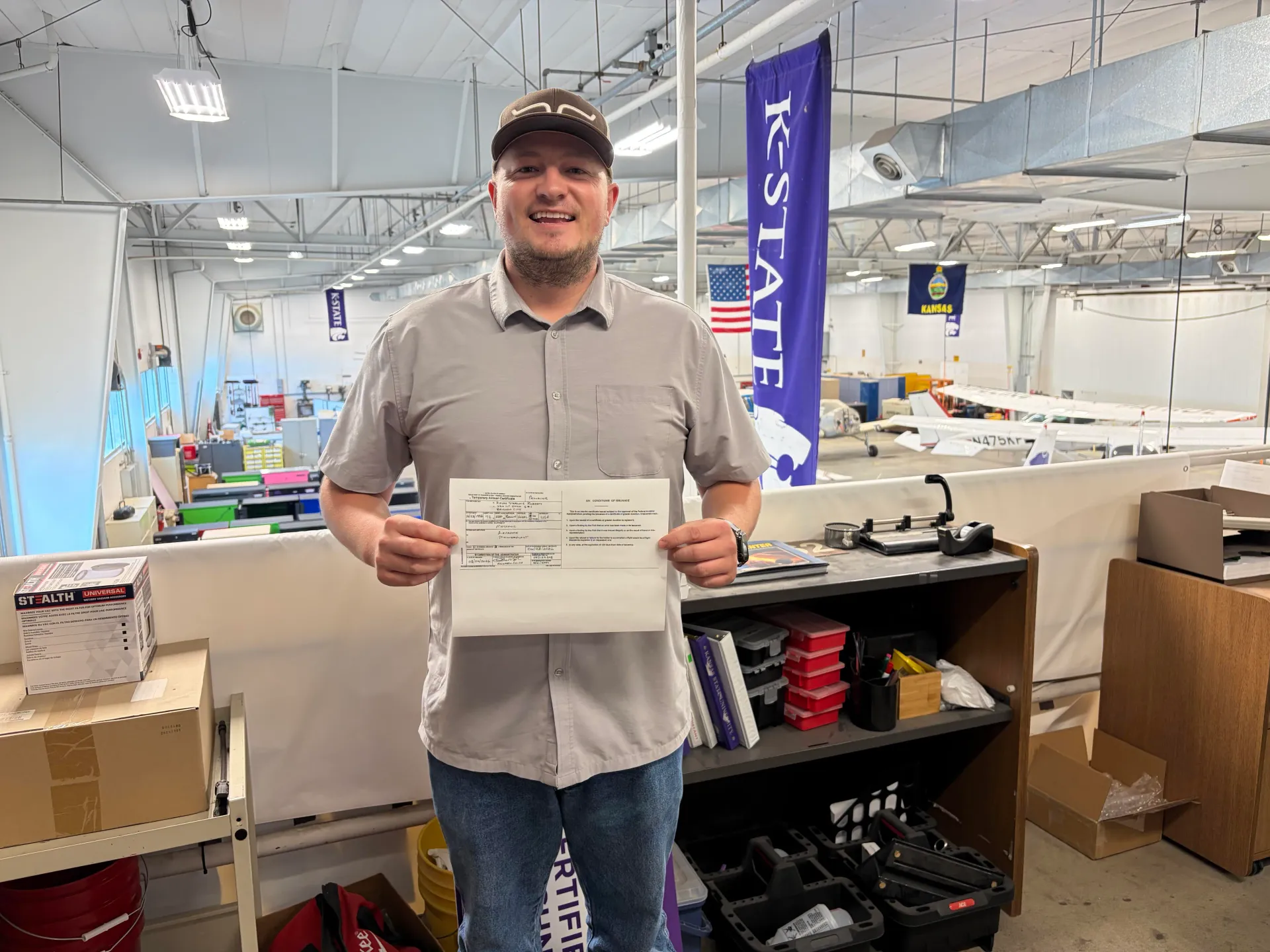 Student holding an aviation certificate inside an aircraft maintenance facility